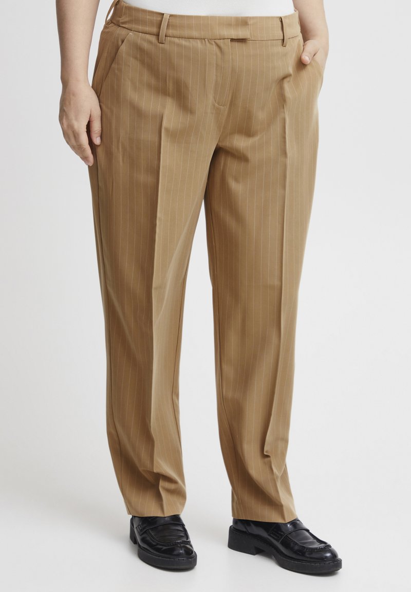 Tan gestreepte broek van een gladde stof, met zijzakken en een ontspannen pasvorm, gecombineerd met zwarte nette schoenen.