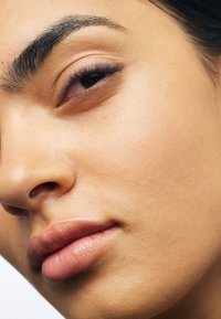 Close-up van een gezicht met een gladde, lichtbruine huid; gedefinieerde wenkbrauwen; en zachte, natuurlijke lippen met een subtiele roze tint.