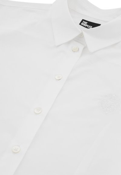 White button-up shirt made of smooth fabric. Features a classic collar, six buttons, and an embroidered logo on the upper left side.