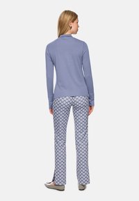 Himmelblaues Langarmoberteil mit Kragen, kombiniert mit gemusterten Palazzo-Hosen in Blau und Weiß, die seitliche Schlitze in der Nähe der Knöchel aufweisen.