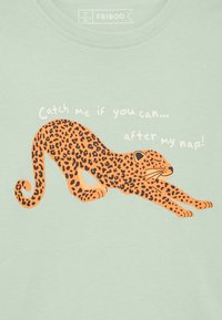 Oranžinis leopardo rašto gyvūnas, besitempiantis su užmerktomis akimis ir tekstu „Pagauk mane, jei gali... po mano miego!“ ant šviesiai žalios medžiagos.