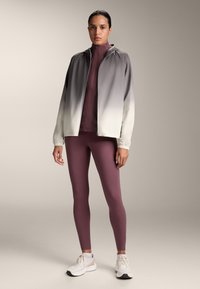 Ľahká bunda s postupným prechodom od sivej po bielu, doplnená tmavoburgundskými legínami a bielymi športovými topánkami. Hladká tkanina a detaily so zipsom.