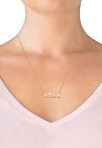 Guld bjergkæde vedhæng på en fin kæde, med skarpe toppe og et minimalistisk design, båret mod en lys rosa top.