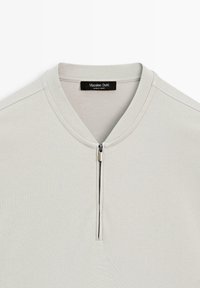 Lysebeige langærmet skjorte med V-udskæring og kort sølvlynlås i midten, med et Massimo Dutti-mærke indeni kraven.