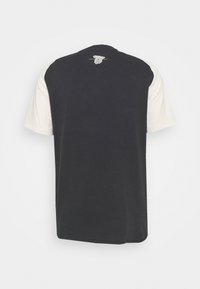 Camiseta de manga corta negra y crema con cuello redondo, un corte relajado y una textura de algodón suave. La vista trasera muestra un diseño de bloques de color.