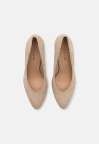 Pompes à bout pointu en suède beige avec une doublure intérieure lisse et un design épuré et minimaliste. L'extérieur présente une texture douce et des lignes nettes.