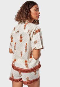 Blusa de manga corta con flores y pantalones cortos a juego en color crema con lunares, que presenta estampados de flores rojas y naranjas y un ribete de patrón contrastante.
