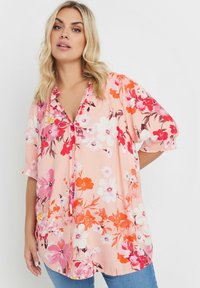 Blusa floreale in tessuto rosa chiaro con fiori vivaci rossi, rosa e bianchi. Vestibilità ampia con scollo a V e maniche corte.