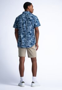 Camisa de manga corta en azul marino con patrones florales, combinada con pantalones cortos khaki. Zapatillas blancas y calcetines completan el conjunto.