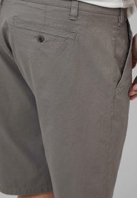 Grijze shorts van zacht stof met een gladde textuur. Voorzien van een achterzak met een knoop en zijzakken voor gebruiksgemak.