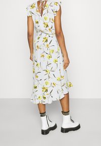 Florales Midikleid in Hellblau mit Rüschenärmeln, einem Bindebändchen am Rücken und einem ausgestellten Saum. Kombiniert mit weißen klobigen Stiefeln.