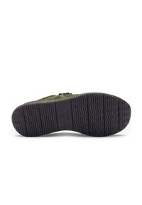 Semelle en daim vert avec un motif en caoutchouc noir texturé, présentant un profil en relief et un nom de marque embouti sur le côté.