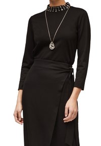 Czarna sukienka z długim rękawem z ozdobnym dekoltem, zawiązywanym paskiem i gładkiego materiału. W skład zestawu wchodzi srebrny naszyjnik z zawieszką.