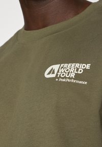 Camiseta de algodón verde oliva con un logo blanco impreso que dice "FREERIDE WORLD TOUR by PeakPerformance" en el frente. Diseño clásico de cuello redondo.