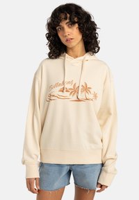 Felpa con cappuccio beige realizzata in morbido tessuto, caratterizzata da un ricamo di un tramonto e palme in colore ruggine. Vestibilità ampia con polsini a costine.