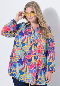 Blusa multicolore con un motivo floreale e a cuori, maniche lunghe, colletto e chiusura a bottoni. Il tessuto ha una texture liscia e leggera.