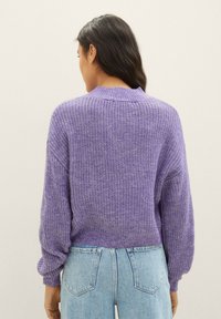 Pull tricoté violet avec une coupe décontractée, col et poignets côtelés, et motif texturé. Associé à un jean taille haute bleu clair.