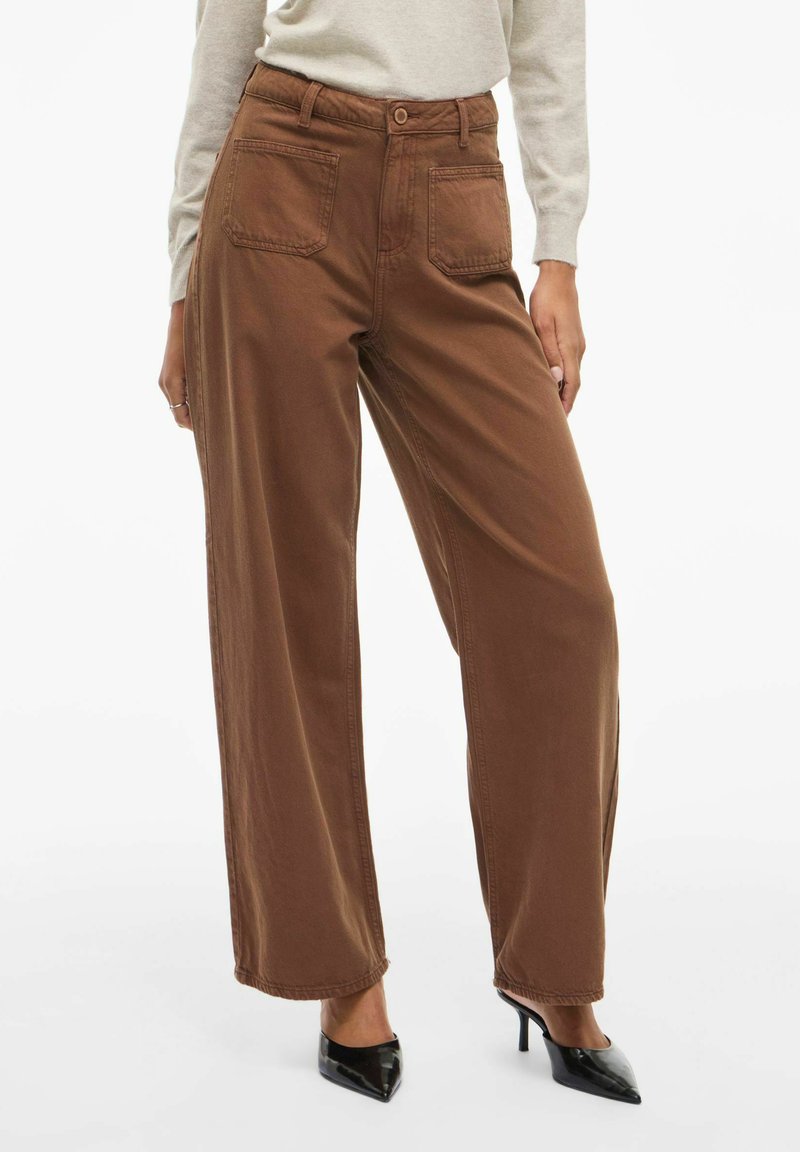 Pantaloni larghi marroni in cotone, con due tasche posteriori, chiusura con bottone e orlo pulito. Abbinati a tacchi neri a punta.