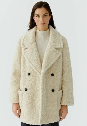 Beige doppelreihiger Mantel aus strukturiertem Stoff, mit großen schwarzen Knöpfen, einem Reverskragen und Taschen an den Seiten.