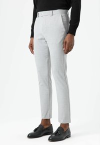 Lichtgrijze, op maat gemaakte broek met een gladde textuur, voorzien van een strakke pasvorm, zijzakken en een enkele voorplooi. Zwarte loafers maken de look compleet.