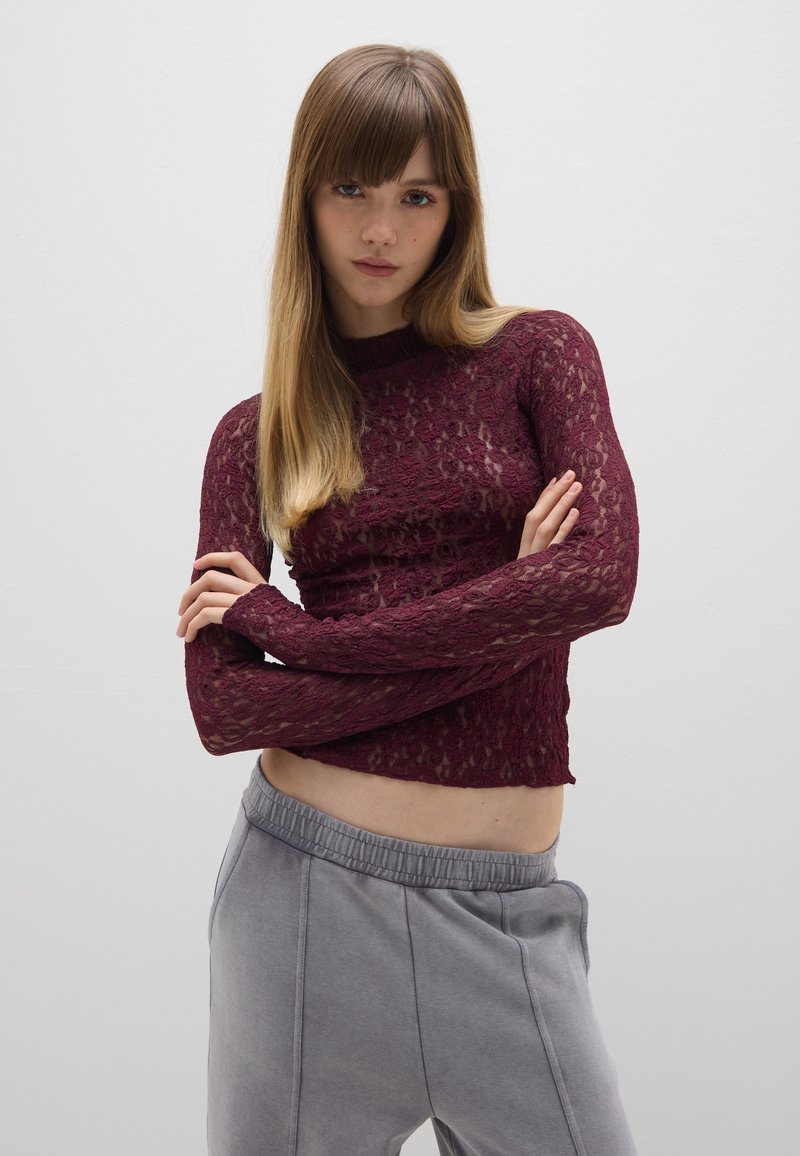 Bordeaux kanten top met lange mouwen en hoge hals, gemaakt van doorschijnend materiaal, gecombineerd met grijze joggingsbroek met elastische taille en zijzakken.