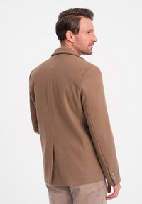 Bruine wollen blazer met een getailleerd silhouet, notch-lapels en twee knopen op de mouwen. Soepele textuur en gestructureerde rug.