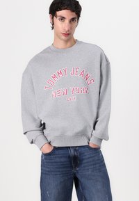Gray sweatshirt made of cotton blend, featuring oversized fit, ribbed cuffs, and "TOMMY JEANS NEW YORK CITY" printed in red on the front.