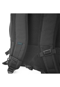 Mochila negra con correas traseras acolchadas de malla. Cuenta con hebillas ajustables y una pequeña etiqueta azul. Tela texturizada con un acabado suave.