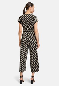 Combinaison noire et beige avec un motif ondulé, manches courtes, coupe ample et jambes larges. Associée à des talons noirs à lanières.