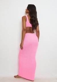 Completo due pezzi in maglia rosa composto da un top corto e una gonna lunga. Tessuto a trama fitta, silhouette aderente che esalta la forma.