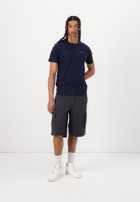 Marineblaues T-Shirt mit kurzen Ärmeln und Rundhalsausschnitt, kombiniert mit grauen Cargo-Shorts mit Seitentaschen und weißen Sneakers mit strukturierter Oberfläche.