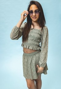 Olijfgroen twee-delige outfit met een smock crop top en een gerimpelde zoom, gecombineerd met een bijpassende rok die een gestructureerd diamanten patroon heeft.