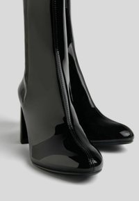 Czarne lakierowane botki za kostkę z eleganckim, spiczastym noskiem, wysokim blokowym obcasem i kontrastowym przeszyciem wzdłuż zamka.