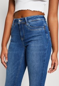 Mørkeblå høy midje jeans laget av denim, med fem-lomme design, subtile slitasjer og messingdetaljer i midjen.