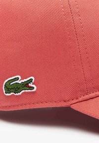 Gorra de béisbol roja con una tela texturizada, que presenta un logotipo de cocodrilo bordado en verde en el lado y una visera curva.