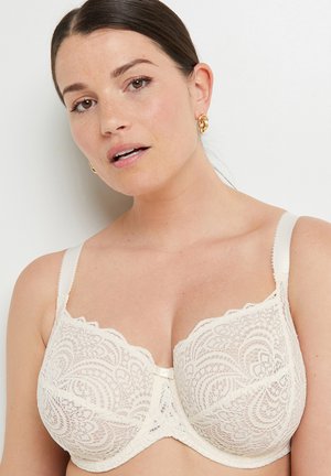 Reggiseno in pizzo di un beige cremoso con bordi scallop, supporto con ferretto e spalline regolabili. Presenta intricati motivi floreali e un accento in nastro di raso.
