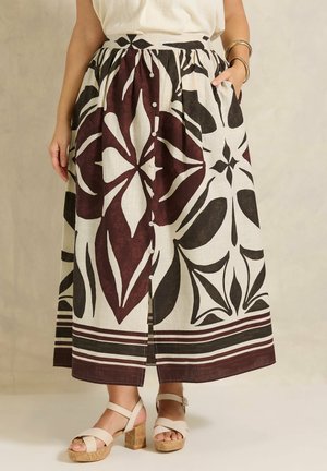 Mid-lang nederdel med store sorte og mørkerøde blomsterprint og knapper foran, båret med beige hælede sandaler og guldbangles.