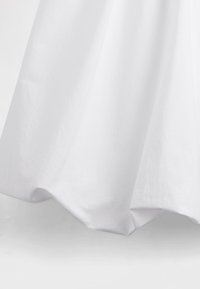 Biele bavlnené oblečenie s jemnou, hladkou textúrou. Má okraj so zubatým lemom, ktorý vytvára mäkký záves smerujúci k zemi.