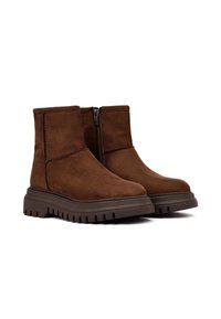Bruine suède enkelboots met een rits aan de zijkant, voorzien van een dikke, geribbelde rubberen zool en eenvoudige stikdetails langs de naden.
