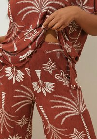 Tvådelad outfit med rustfärgad tyg med vita palmblad och diamantmönster. Inkluderar en lös topp och matchande byxor. Strukturerad väv.