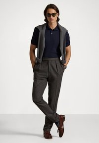 Μπλε ναυτικό πόλο πουκάμισο συνδυασμένο με γκρι πλεκτό γιλέκο και καλοραμμένο γκρι παντελόνι. Καφέ δερμάτινα παπούτσια ολοκληρώνουν το σύνολο. Ορατές λείες υφές υφασμάτων.