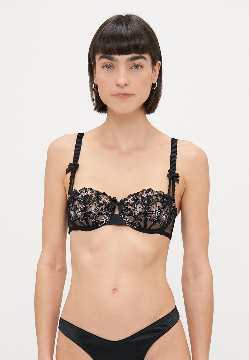 Mustat pitsiset rintaliivit kukkakirjailulla, läpinäkyvät kupit ja musta satiinivuori. Varustettu säädettävillä uritetuilla olkaimilla, joissa on solmukset.