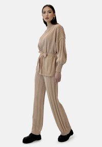 Beżowy zestaw odzieży domowej wykonany z dzianiny, z pionowym prążkowanym wzorem, długimi rękawami, paskiem w talii oraz szerokimi spodniami z elastycznymi mankietami.