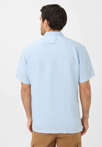 Camicia azzurro chiaro a maniche corte con colletto casual, tessuto testurizzato e orlo dritto, dotata di una piccola apertura posteriore e spacchi laterali.