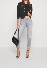 Černá zkrácená džínsová bunda přes přiléhavý černý top, párovaná se světle šedými vysokými džíny s ohrnutými manžetami a černými páskovými podpatky.