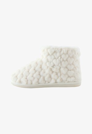 Zapatilla suave blanca hasta el tobillo con textura de felpa estampada con corazones y suela plana, diseñada para la comodidad y el calor en interiores.