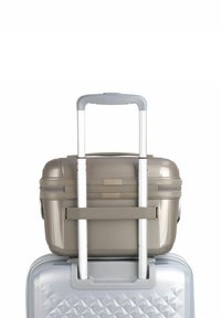 Set di valigie rigide con un caso superiore grigio dotato di cerniere e un caso inferiore beige con superficie texture e manico retrattile.