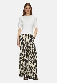 Haut blanc à manches courtes associé à un pantalon large à motifs géométriques noir et crème, avec une coupe décontractée et des poches latérales.