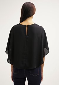 Sort kappe-stil bluse lavet af letvægtsstof, med en nøglehul rygdetalje og flydende silhuet. Rene kanter og ingen synlige lukninger.