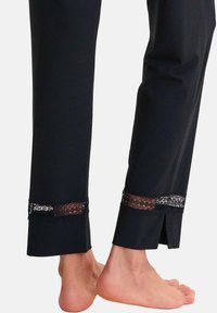 Pantalons noirs à coupe droite, dotés d'une bordure en dentelle transparente à l'ourlet et de fentes latérales ouvertes. Le tissu doux offre une texture lisse.